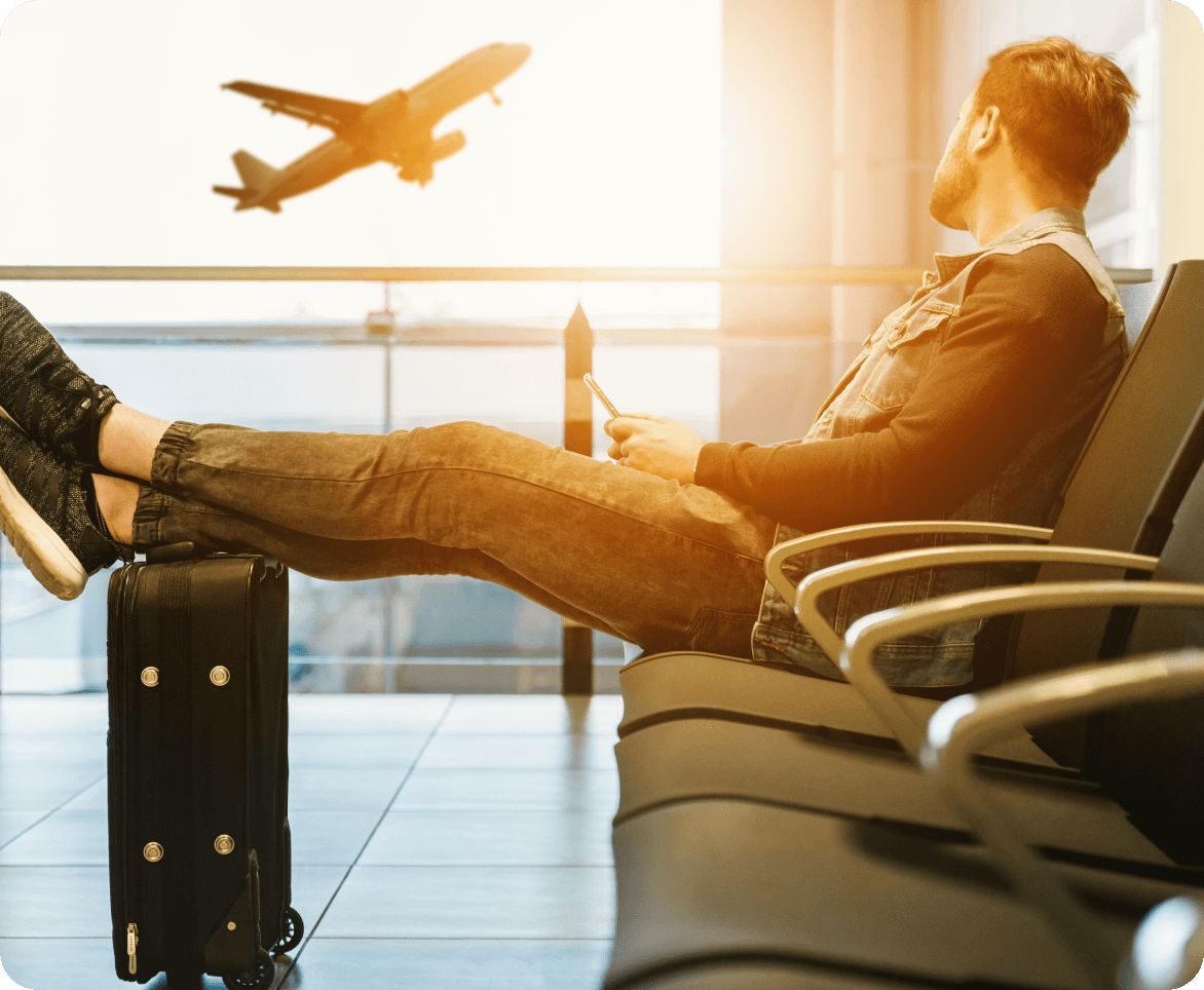 A man sits in an airport with his feet up as a plane takes off in the background.